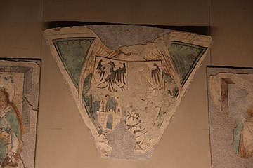 Triangle on which a shield is painted. The latter is divided into four. On the first part on the upper left there is a black bird on a white background, the same on the upper right but erased, on the lower left there is a white castle on a blue background and the last drawing is barely visible.