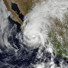 A photograph of a hurricane near the Pacific coast of Mexico; its eye is mostly obscured by clouds, and there is a large shield of clouds extending to the north and distant northeast of the center