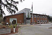 A brown building with two stories, a large glass atrium, and a flagpole.