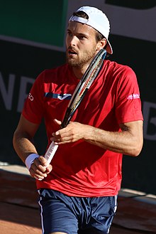 João Sousa in a white shirt and cap looks down before a serve