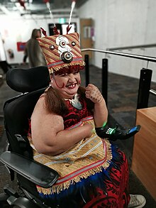 Lusi is sitting in her chair in traditional Samoan costume, smiling at the camera