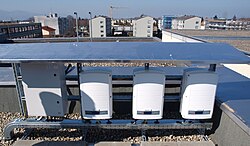 A group of three white SolarEdge inverter boxes on the roof of a high school in Austria