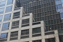 Detail of the rebuilt facade of the Kress Building as seen on Fifth Avenue. The lower wall of marble ascends like a staircase in front of the upper wall, which is made of glass.
