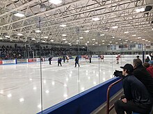 Interior view of arena showing the ice surface, seating area and a youth hockey game