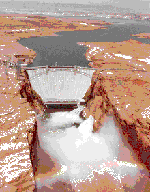 Glen Canyon Dam releasing floodwater. A rainbow is visible over the Colorado River.