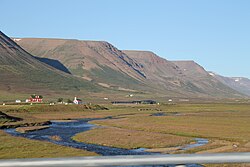 The Hofsá river running through a flat area, with a few scattered buildings and mountains in the background