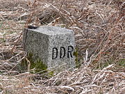 Square grey stone in scrubby brown grass with "DDR" carved on the right face.