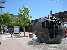 People walking outside a single storey brick building with metal globe sculpture and library sign