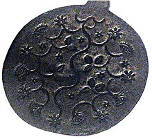Round metal plate decorated with raised pattern of flowers, vines, and leaves