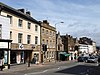 Street scene showing shops, cars and a set of traffic lights.