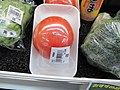 A tomato on a plastic tray and with a plastic shrink film