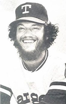 A man in a light baseball jersey and dark cap