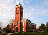 A red brick building with a tall tower, situated against a mostly clear sky