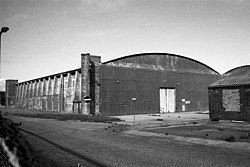 A black and white image of an aircraft hangar in a semi-derelict state