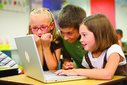 Three young students seated and viewing a laptop in a classroom