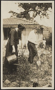 Marion Mahony Griffin on the left with a watering can and Walter Burley Griffin with a shovel in front of a small building