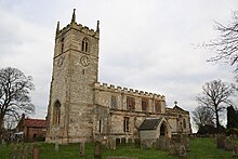 A stone church seen from the southwest. On the left is the tower with a battlemented parapet and pinnacles, in the centre is the nave, also battlemented, and to the right at a lower level is the chancel