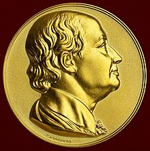 A golden medallion with an embossed image of Mikhail Lomonosov facing left in profile.