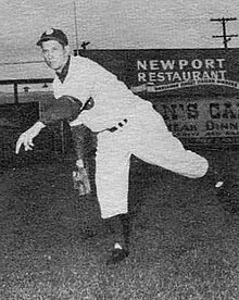 A man in a light baseball uniform and a dark cap shown just having thrown a ball