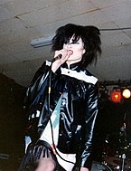 一个戴着黑假发，穿着黑白乡间的夹克对着麦克风唱歌的女性。
