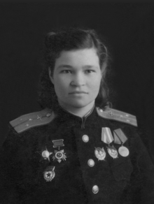 Photo of Sebrova wearing her medals including her guards pin, Order of the Red Star and an Order of the Patriotic War on the right side of her chest (left in image); on the other side her Hero of the Soviet Union Gold Star is pinned above the first row of four medals with her Order of Lenin and three orders of the Red Banner. Two campaign medals, one for the defense of the Caucuses and one for Victory over Germany are below the row of Orders of the Red Banner.