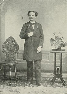 A black and white image of Mary Walker wearing a suit and standing facing the camera with her right hand tucked into her jacket.