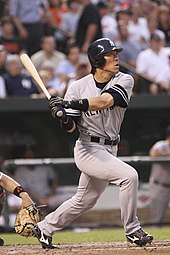An Asian male wearing a gray uniform with the lettering "NEW YORK" across it, in his after-swing pose.