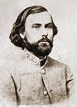 Photo shows a stern, bearded man with long hair wearing a gray military uniform with general's stars on the collar.