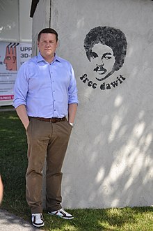 Tobias Baudin standing beside a mural depicting Dawit Isaak with "free dawit" written below