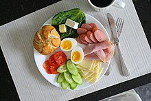 Plate of veggies, bread, meats, cheese, and a sliced, soft-boiled egg.