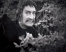 An actor dressed as a vampire surrounded by bushes