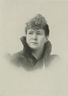 B&W portrait photo of a middle-aged woman with her hair in an up-do wearing a high-collared dark jacket.