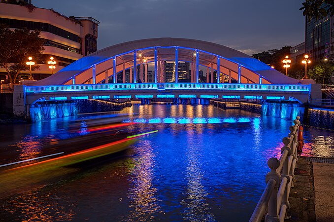 图为在华灯初上时通过新加坡爱琴桥的船只。
