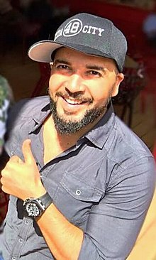 Abdelhafid Douzi wearing a gray shirt and ballcap, holding a thumbs-up, smiling at camera