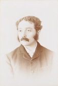 Neil, a young-ish man with a buttoned-up coat, a moustache and sideburns.