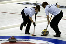 Two female curling players on the field, using their brushes.