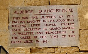 A plaque with the inscription AUBERGE D'ANGLETERRE: THIS WAS THE AUBERGE OF THE ENGLISH KNIGHTS. IN THE ADJOINING BUILDING LIVED OLIVER STARKEY LATIN SECRETARY TO GRAND MASTER VILETTE AND TURCOPILIER OF THE ORDER AT THE TIME OF THE GREAT SIEGE IN 1565