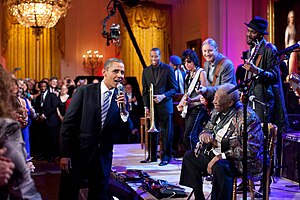 Color photo of Barack Obama singing into a microphone with B.B. King and other musicians and guests.