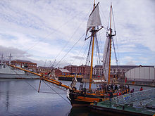 A boat with large sails is pictured in a harbor.