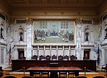The chamber of the Wisconsin Supreme Court is a large, orante room, where judges sit behind a long desk beneath a large mural depicting the founding fathers signing the US Constitution, in front of a table for attorneys.