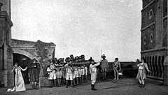 A row of soldiers, left, aim their rifles at a lone figure, right, while (centre) an officer raises his sword as a signal. An agitated woman, extreme left, turns her face from the scene.