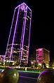 A view of the bank of the America Plaza in Dallas. It's lit up in purple, with sidewalk decorations in the foreground.