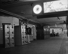 Black and white image of the uptown IRT platform in 1978. There are lockers to the left and a clock hanging above the platform.