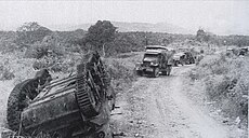 French vehicles lay abandoned or destroyed. An M8 75 mm howitzer motor carriage is overturned on left