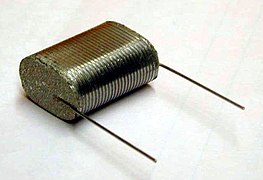 Flattened winding of a "naked" film capacitor before encasement, with a view of collateral metal contact layers ("schoopage") and attached terminals