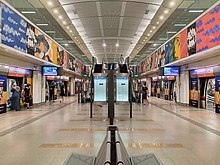 The island platform of Buangkok station featuring a line map and benches, with the station artwork adorned above the platform screen doors. At the centre of the image, escalators, and stairs lead to the upper level of the concourse.