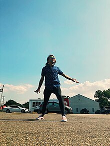 Photo of Carmen Shields with their hands out and standing in a peacefully excited stance.