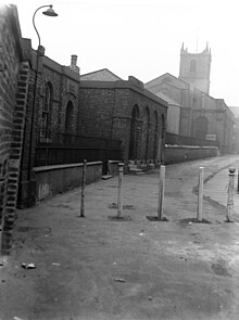 several brick buildings on the left hand side of the photograph with a row of bollards dividing the photo in half horizontally. Very faintly, one can see a sign above a door of one of the brick buildings reading 'The Donnison School'