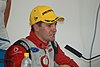An young aged man is wearing a yellow baseball cap with sponsors logo and a red and white racing overalls