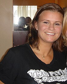 A young woman with brown hair smiles in front of a camera.